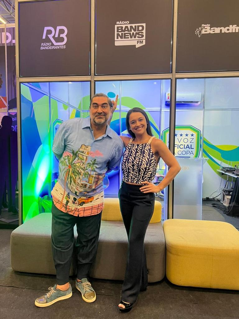 Zeca Camargo e Carla Bigatto em frente ao estande das rádios BandNews FM e Bandeirantes BandNews FM